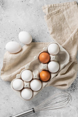  Eggs in a tray on the kitchen table. White and brown eggs and a whisk for baking. Chicken eggs and a whisk on a culinary background. Concept of preparation for baking. Top view with space for text