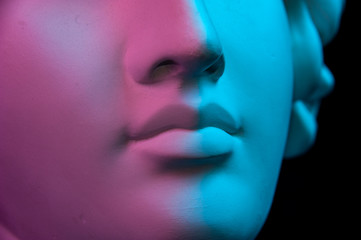 Colorful gypsum copy of ancient statue of human head for artists on a black background. Close up view lips. Plaster sculpture of human face. Toned blue and purple. Webpunk, surreal style poster.