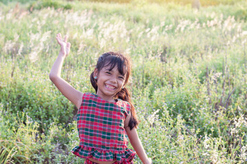 Asian little girl wore a dress made of Thai loincloth or Kamar band or Commer band standing and laugh bright in the fields on a sunset evening in the countryside.