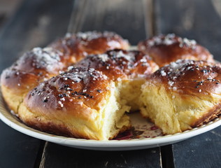 Homemade cake.Buns, sprinkled with sesame and sugar syrup, in a white plate on a dark wooden table.