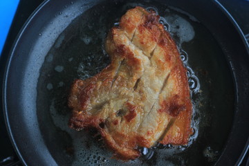 Fried marinated pork  steak in frying pan, close up view.