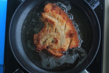 Fried marinated pork  steak in frying pan, close up view.