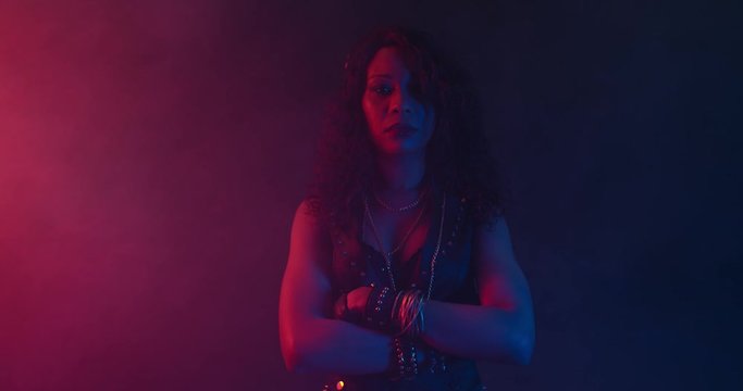 Black woman with her arms crossed is standing in colorful lights and the smoke