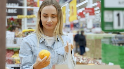 Young woman is selecting fresh orange at grocery store.