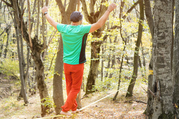 Naklejka na ściany i meble A bearded man aged walks along a slackline in the autumn forest on a sunny afternoon. The concept of Leisure and Recreation of active middle-aged people