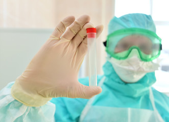 A doctor in a protective suit holds a test tube in his hand,close-up.