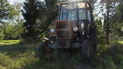 Old tractor founded in the grove. Vintage agricultural machine waiting in the shadows.