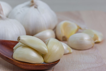 Brown wooden spoon with peeled garlic slices