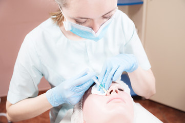 A female beautician makes an injection to a female client in a cosmetics office. Cosmetic procedures for rejuvenation