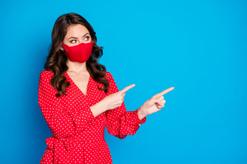 Photo of attractive lady responsible citizen keep social distance direct fingers empty space wear dotted red dress protective facial respiratory mask isolated blue color background