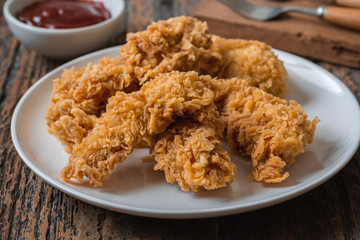 Crispy fried breaded chicken strips on plate and ketchup.