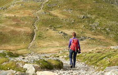 A hiker descending the rocky path from Brim Fell and walking towards Dow Crag on a sunny Day in the Lake District.