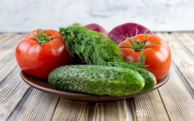 On a plate are vegetables, tomatoes, cucumbers, onions and dill. Fresh vegetables close-up. Natural food.
