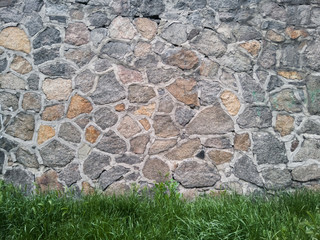 Old textured stone wall with grass below.