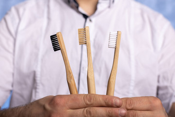 Three bamboo toothbrushes in male hands close-up. eco friendly. biodegradable hygiene items. multi-colored bristles. place for text