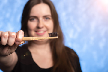 eco-friendly bamboo toothbrush in a female hand. girl with a snow-white smile on the background in defocus. oral hygiene. items from biodegradable materials. close-up.
