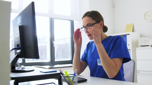 medicine, technology and healthcare concept - tired female doctor or nurse in glasses with computer working at hospital