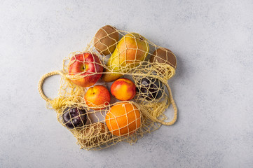 Fruits in the range in yellow eco string bag on a light wooden surface. Environmental protection concept. Top view