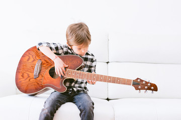 Young man playing guitar sitting on sofa on white background copy space.