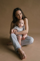 Beautiful portrait of mother and child in dark tones. Stylish prety brunet young woman with baby boy toddler playing smiling hug in studio. Love and tender feelings