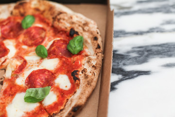 Fresh Italian pizza in a paper box. Margarita with melted mozzarella  with basil leaves on top. Marble table background with space for text