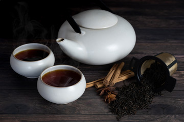two cup of tea, teapot, cinnamon stick, tea strands, strainer, star anise on wooden table.