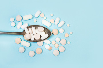 Medicamentos en pastillas sobre una cuchara de metal sobre un fondo azul liso y aislado. Vista...