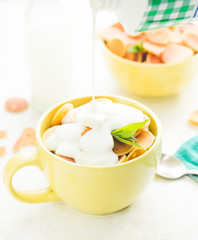 Mini pancake cereal in light green mug, white concrete background ready to serve on breakfast. New food trend. Copy space for text. Butter and mint leaves, milk, checkered aqua cloth, flowing yogurt