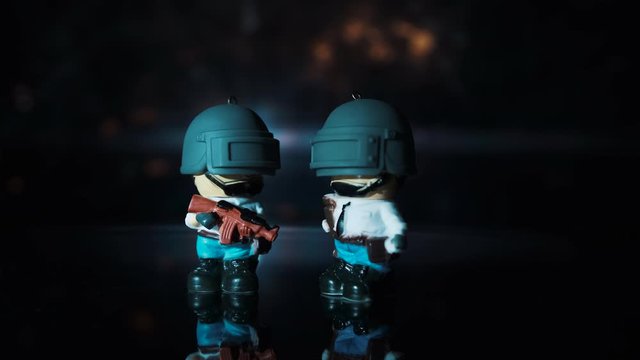 Two little man from the game with a rifle stands on a table against the color background
