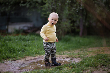 a little boy in rubber boots plaing in the puddle