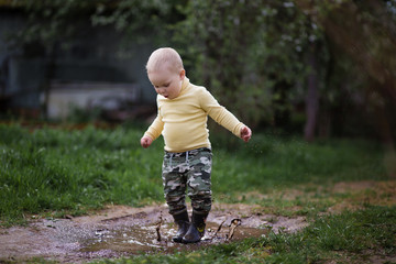 a little boy in rubber boots running in the puddle