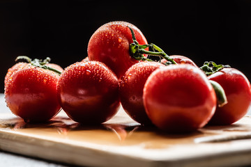 fresh ripe red tomatoes on branch with water drops on wooden board isolated on black