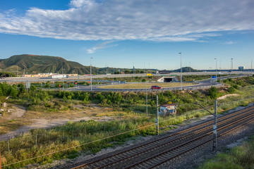 Fototapeta na wymiar Train tracks, road A-2 and roundabout access, with Ecce Homo hill in the background, just outside Alcalá de Henares on a spring afternoon.