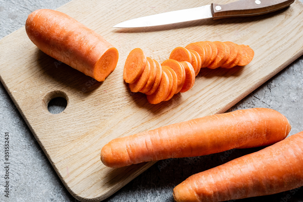 Wall mural fresh ripe carrot slices on wooden cutting board with knife on concrete surface