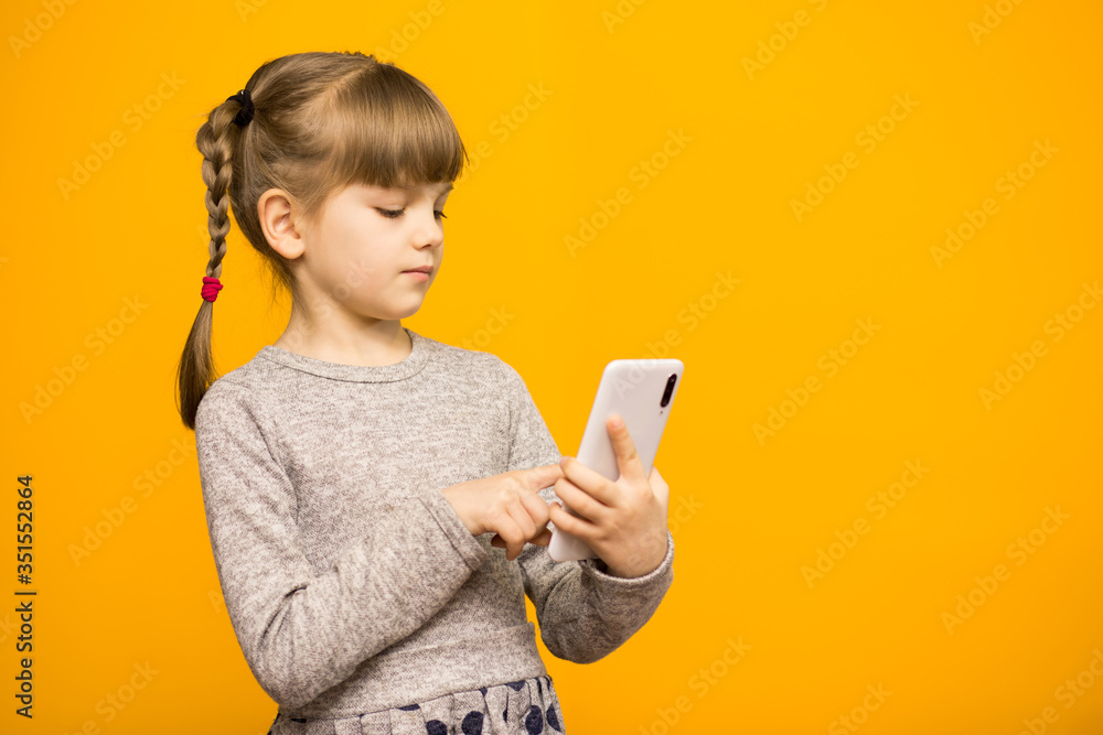 Wall mural Child girl text messaging with mobile phone isolated over yellow