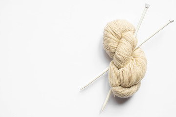 top view of beige yarn and knitting needles on white background with copy space