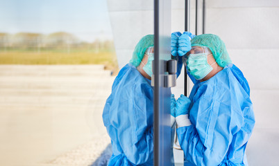 Exhausted doctor in protective clothing leans on door because of stress and exhaustion