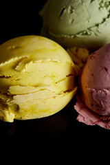 close up view of delicious yellow, pink and green ice cream balls isolated on black