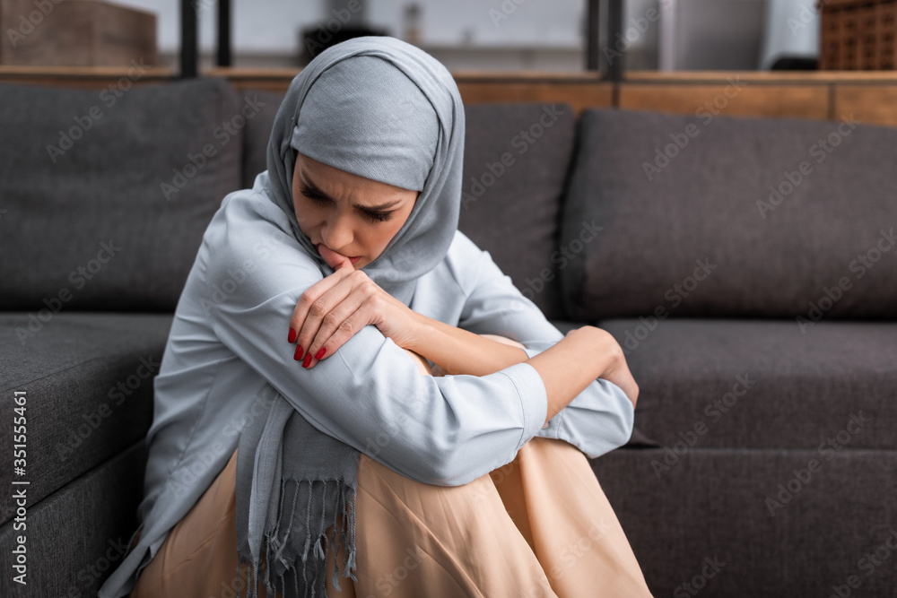 Wall mural sad arabian woman in hijab sitting on floor in living room, domestic violence concept