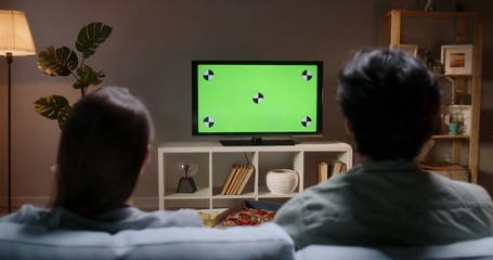 Unrecognizable couple sitting together on couch at home, watching tv shows with chroma-key green screen and eating unhealthy food 4k footage template - Powered by Adobe