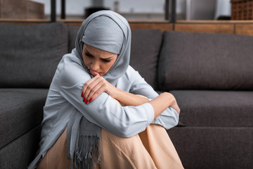 sad arabian woman in hijab sitting on floor in living room, domestic violence concept