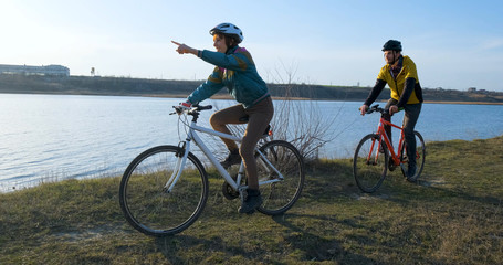 Fototapeta premium Couple of male and female ride on bicycles near river during sunset 