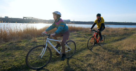 Couple of male and female ride on bicycles near river during sunset	