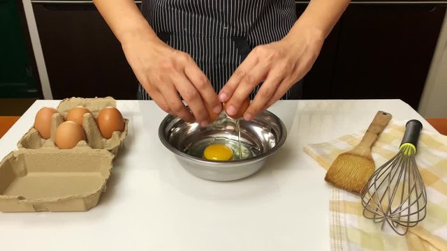 Female hands cracking an egg over silver bowl. 4K video.