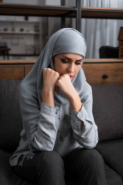 upset muslim woman in hijab sitting on sofa, domestic violence concept