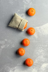 Mandarin citrus fruits row, one in a burlap bag. Flatlay on grey cement background.