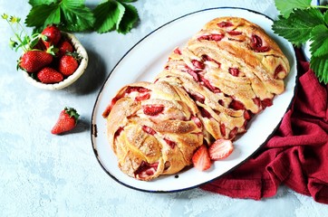 Yeast babka with strawberries and sugar in a dish on a gray background