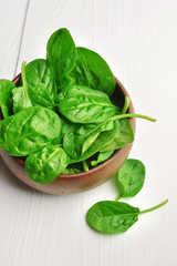 Fresh spinach leaves in wooden bowl over white wooden table. Healthy vegan food. Green living and eco-conscious concept.