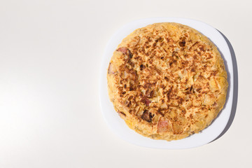 Authentic homemade Spanish omelette made with eggs, potatoes and bacon. Traditional Spanish cuisine. Food and gastronomy concept. Homemade and traditional. Copy space. White background. Top view.