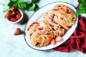 Yeast babka with strawberries and sugar in a dish on a gray background